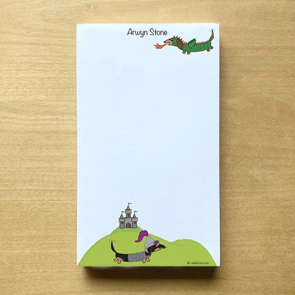One dachshund dressed as dragon and the other as a knight with medieval castle in background in this  personalized and unlined notepad