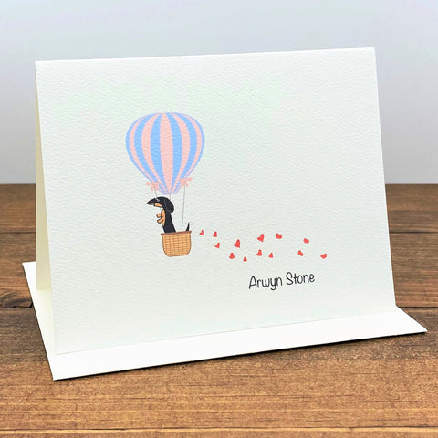 Personalized note card with black and tan dachshund in hot air balloon with trail of hearts behind it.