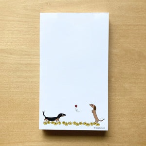 Two dachshunds playing in field of yellow flowers with ladybug in this unlined notepad