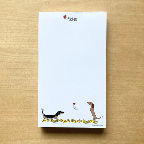 Two dachshunds playing in field of yellow flowers with ladybug in this personalized unlined notepad