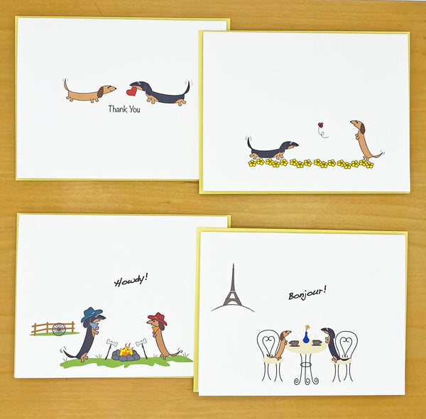 Dachshund assorted note card set, two dachshund facing each other one holding a heart, two dachshunds playing in field of yellow flowers with ladybug, two dachshunds wearing cowboy hats with "Howdy" message on front, two dachshunds in Paris Cafe drinking coffee with Eifel tower in background and "Bonjour" message on front of card