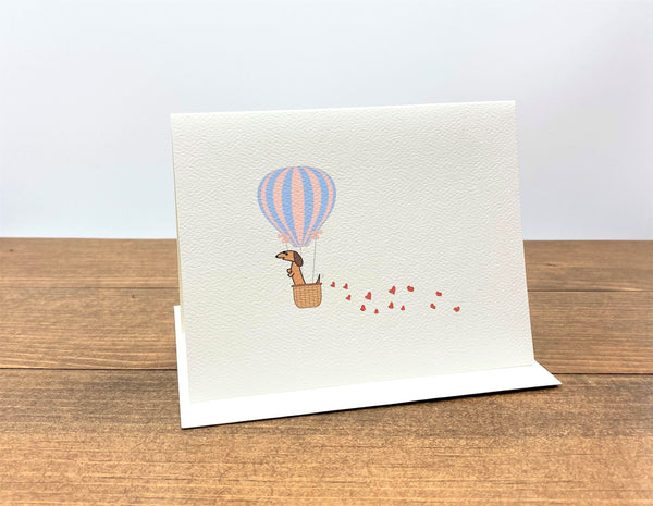Note card featuring dachshund in hot air balloon with hearts trailing behind