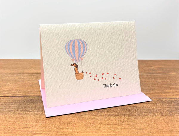 Thank you note card featuring dachshund in hot air balloon with hearts trailing behind