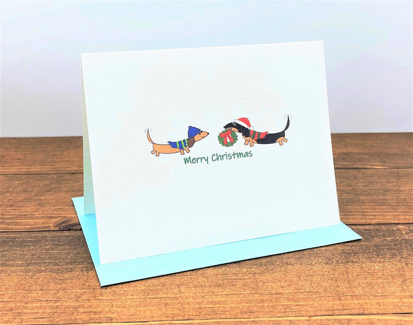 Two dachshunds wearing hats and scarves with wreath Merry Christmas Card