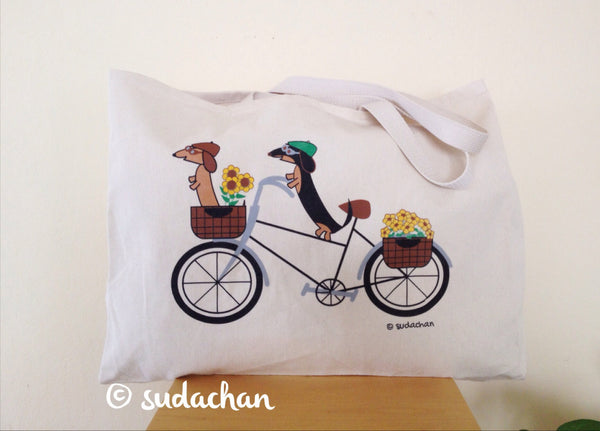 Large  screen printed cotton twill tote bag with two dachshunds wearing riding caps and goggles on a bicycle with baskets of flowers on the bike.